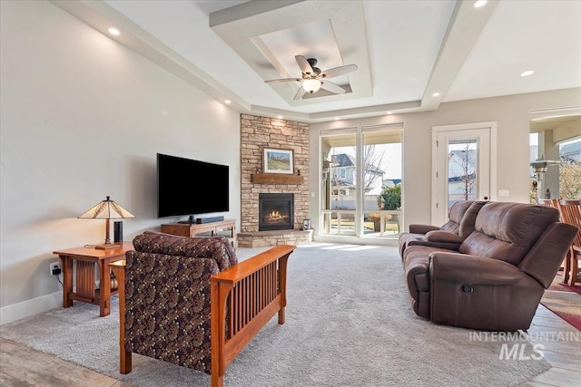 living room featuring ceiling fan, light colored carpet, a tray ceiling, and a stone fireplace