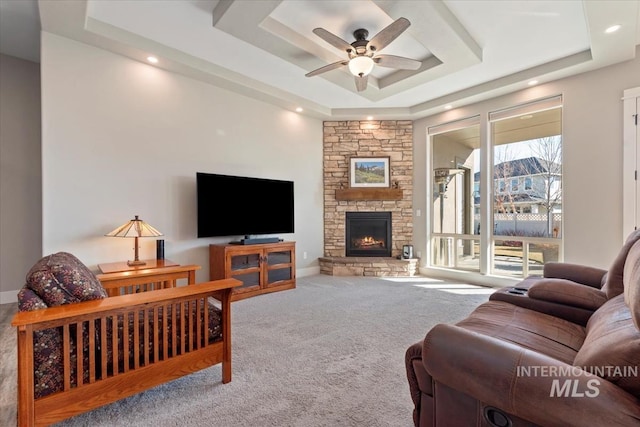 living room featuring a raised ceiling, carpet, a stone fireplace, and ceiling fan