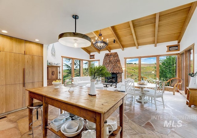 dining area with wood ceiling, a stone fireplace, an inviting chandelier, and vaulted ceiling with beams