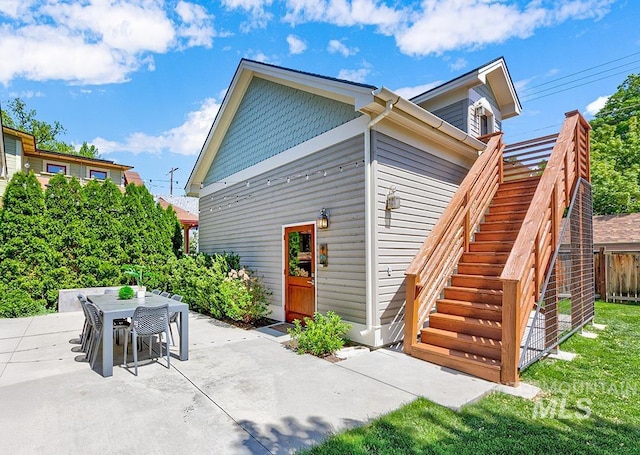 rear view of house with a patio area, outdoor dining area, stairway, and fence