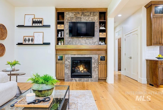 living room featuring wood finished floors, a tiled fireplace, baseboards, recessed lighting, and built in features