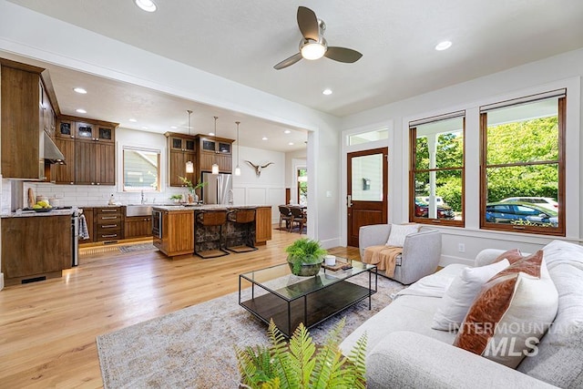 living area with light wood-type flooring, ceiling fan, recessed lighting, and a wainscoted wall