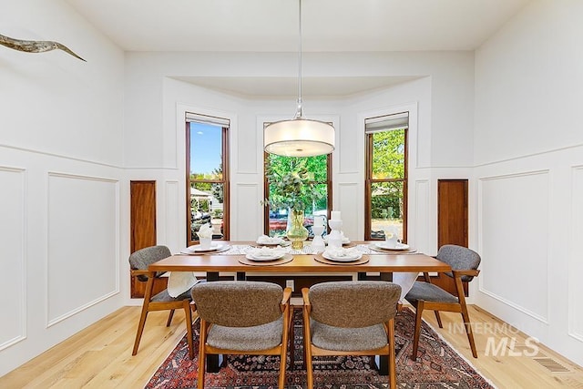 dining space featuring a decorative wall, light wood-style flooring, and a wainscoted wall