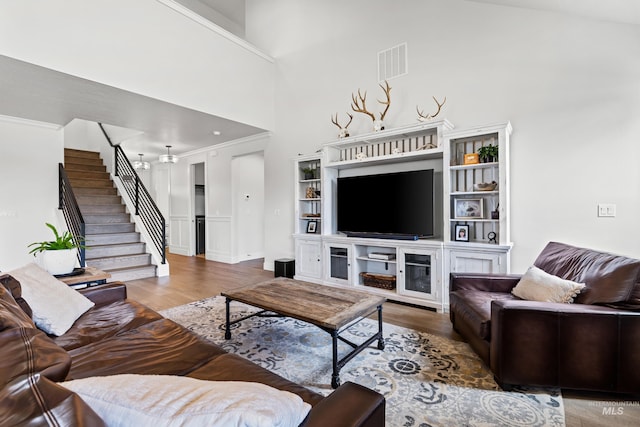 living area featuring a towering ceiling, visible vents, wood finished floors, stairway, and ornamental molding