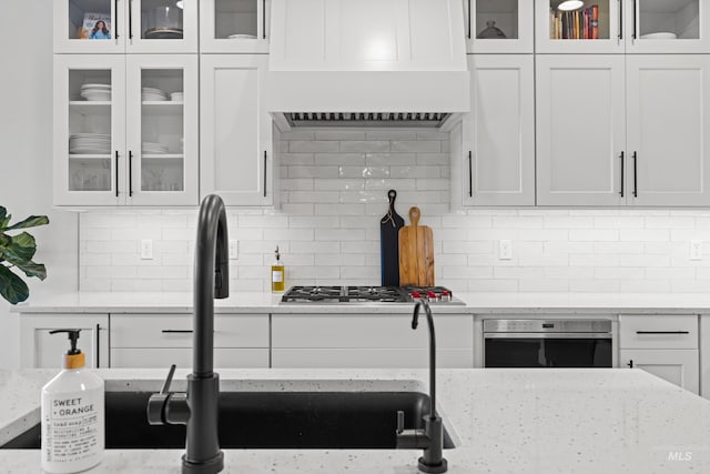 kitchen featuring white cabinetry, light stone countertops, and custom range hood