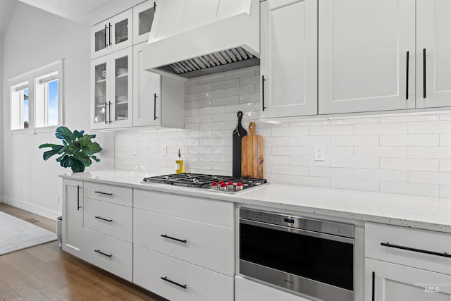 kitchen featuring light stone counters, stainless steel gas cooktop, white cabinetry, custom range hood, and dark wood-type flooring