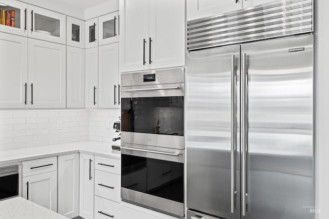 kitchen featuring appliances with stainless steel finishes, tasteful backsplash, light stone counters, white cabinets, and glass insert cabinets