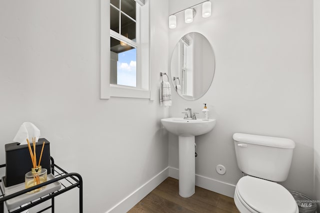 half bath featuring a sink, baseboards, toilet, and wood finished floors