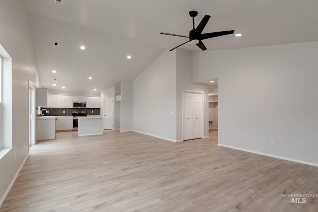 unfurnished living room with ceiling fan, high vaulted ceiling, sink, and light wood-type flooring