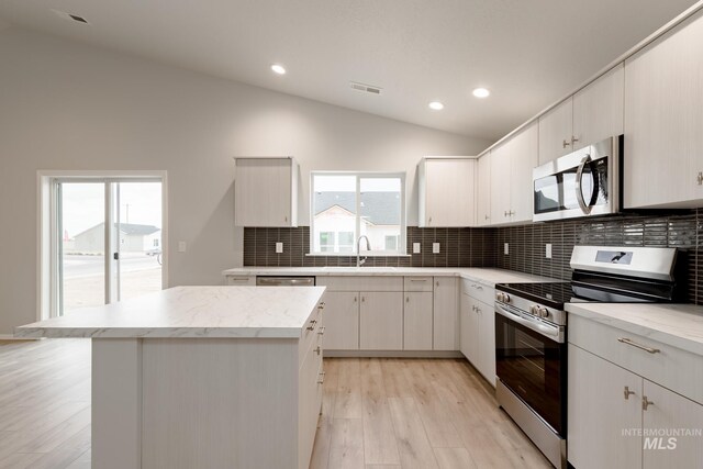 kitchen with appliances with stainless steel finishes, white cabinets, a healthy amount of sunlight, and vaulted ceiling