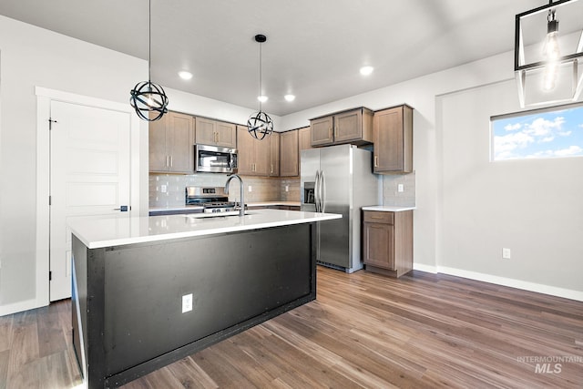 1755 N Crystal Cove Ave, Meridian, ID 83646 - kitchen featuring appliances with stainless steel finishes, decorative backsplash, light countertops, wood finished floors, and a kitchen island with sink
