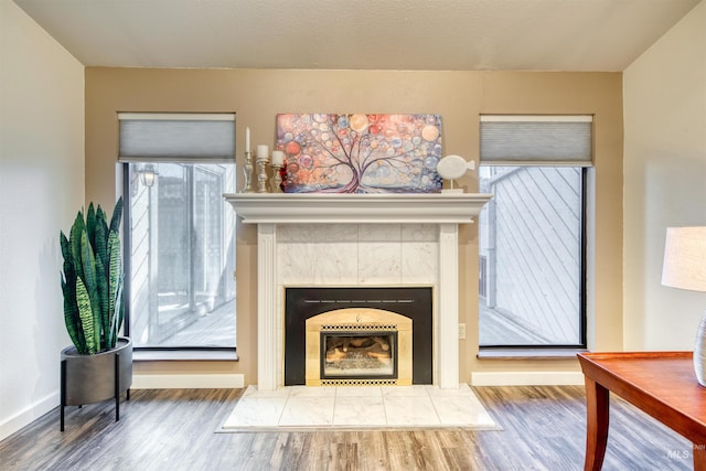 unfurnished living room featuring a tiled fireplace, wood finished floors, and baseboards