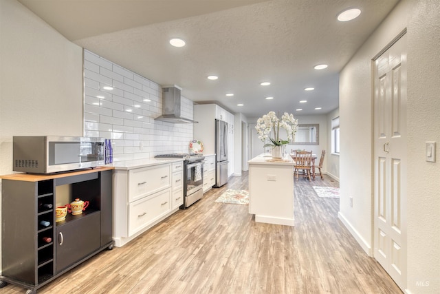 kitchen featuring appliances with stainless steel finishes, wall chimney range hood, white cabinets, and light wood-style floors