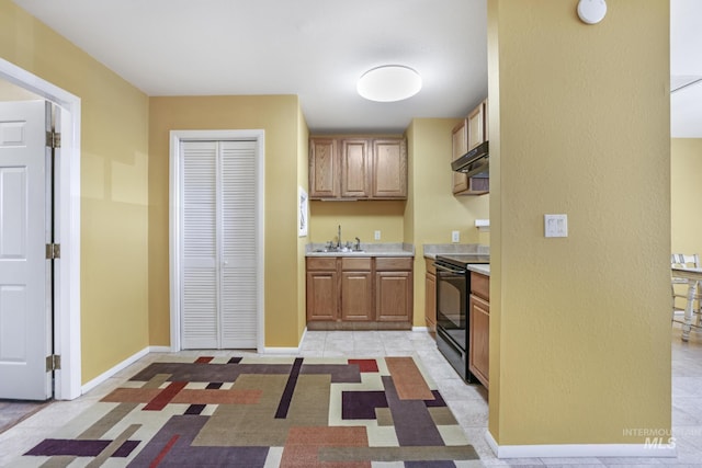 kitchen featuring black range with electric cooktop, a sink, light countertops, under cabinet range hood, and baseboards
