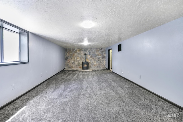 below grade area featuring a wood stove, a textured ceiling, carpet flooring, and baseboards