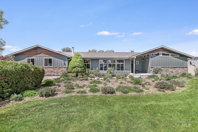 back of property with stone siding, a yard, and board and batten siding