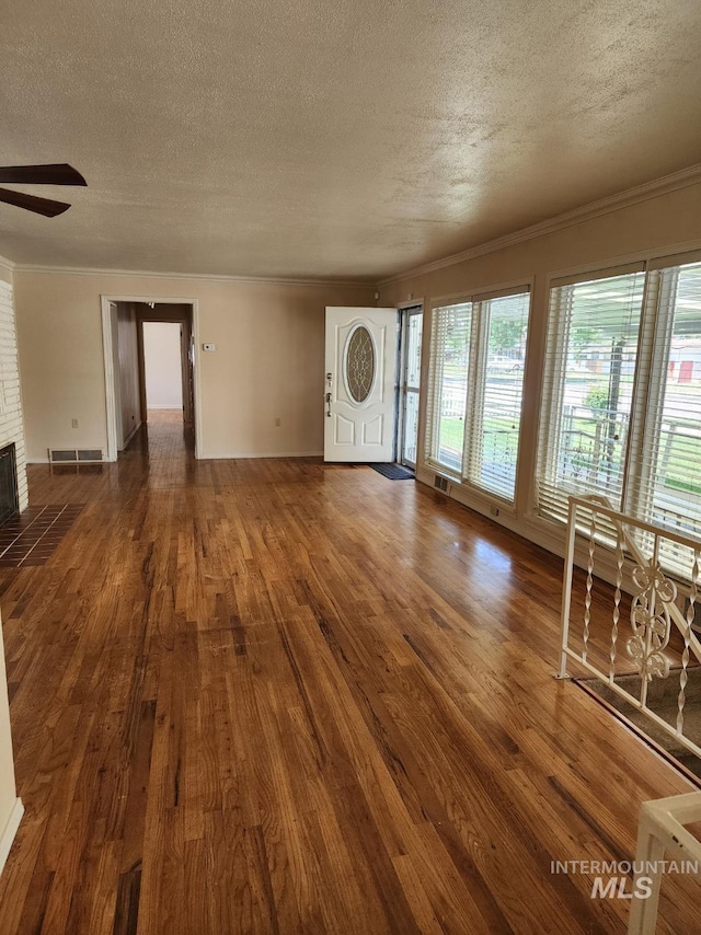 855 N 9th E, Mountain Home, ID 83647 - unfurnished living room featuring a textured ceiling, dark wood-type flooring, a ceiling fan, ornamental molding, and a brick fireplace