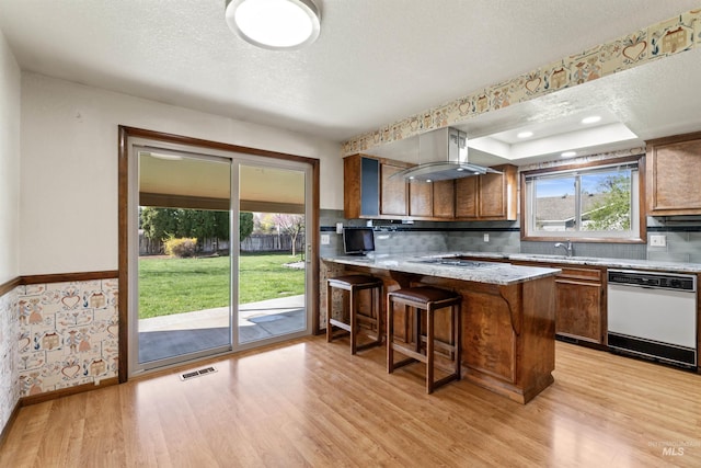kitchen with light wood finished floors, a sink, visible vents, white dishwasher, and range hood