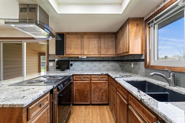 kitchen featuring light wood finished floors, a sink, backsplash, black / electric stove, and range hood