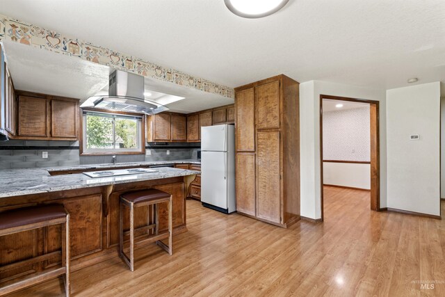 kitchen featuring tasteful backsplash, island range hood, white appliances, light wood finished floors, and a peninsula