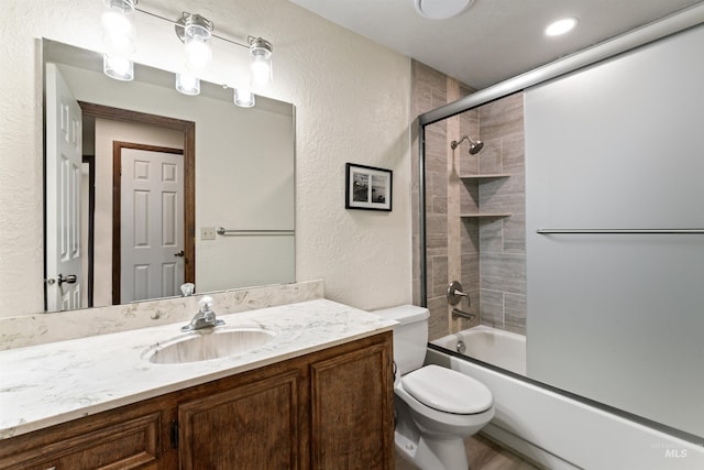 full bathroom featuring toilet, a textured wall, vanity, and combined bath / shower with glass door
