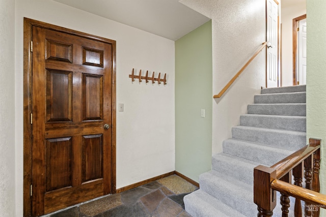 foyer featuring stone tile floors, baseboards, and stairs