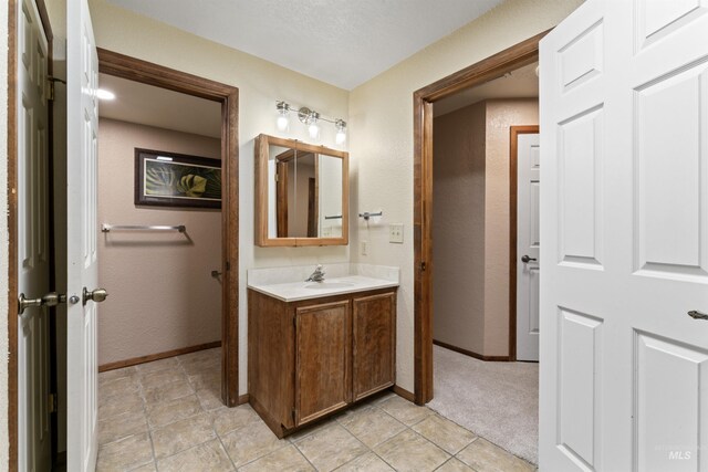 bathroom with a textured wall, baseboards, tile patterned flooring, and vanity