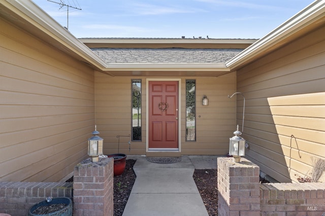 view of exterior entry with roof with shingles