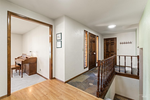 hallway featuring baseboards, wood finished floors, and an upstairs landing