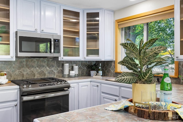 4130 S Ticonderoga Way, Boise, ID 83706 - kitchen featuring appliances with stainless steel finishes, white cabinetry, backsplash, glass insert cabinets, and tile counters