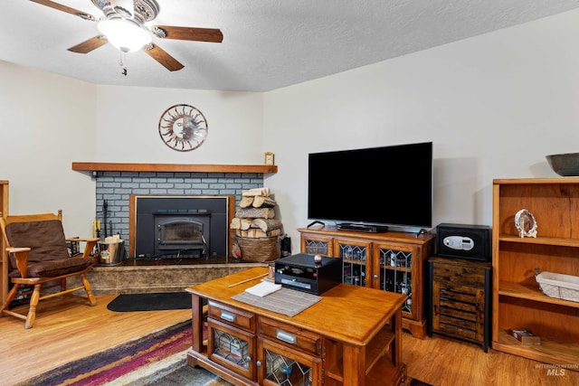 living area with a textured ceiling, ceiling fan, wood finished floors, and a wood stove