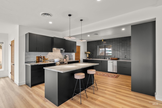 kitchen featuring light wood finished floors, stainless steel appliances, visible vents, backsplash, and dark cabinetry