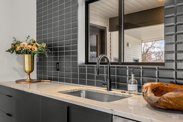 kitchen with tasteful backsplash, dark cabinets, light stone counters, and a sink