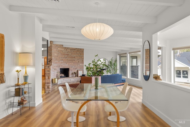 dining room featuring beamed ceiling, light wood-style floors, a stone fireplace, and baseboards