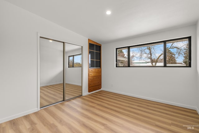 unfurnished bedroom with baseboards, light wood-type flooring, multiple windows, and a closet
