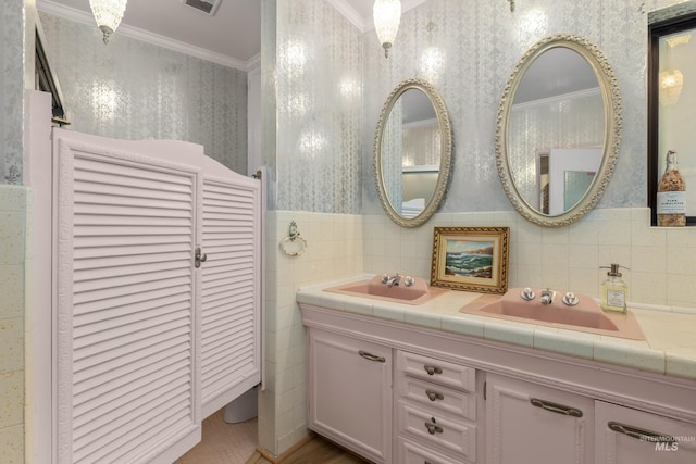 bathroom with crown molding, double vanity, a sink, and wallpapered walls