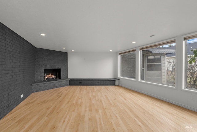 unfurnished living room with brick wall, recessed lighting, wood finished floors, and a brick fireplace