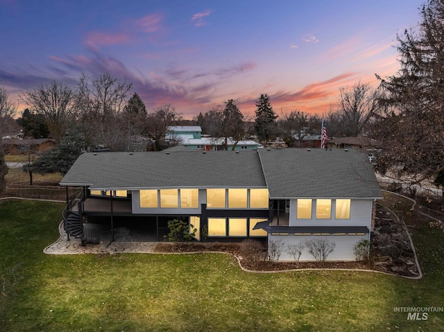 back of house at dusk featuring stairway, a shingled roof, and a lawn