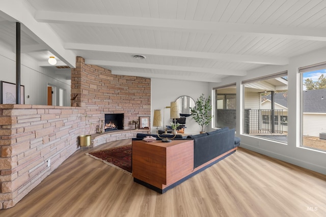 living room with beamed ceiling, wood finished floors, and a stone fireplace