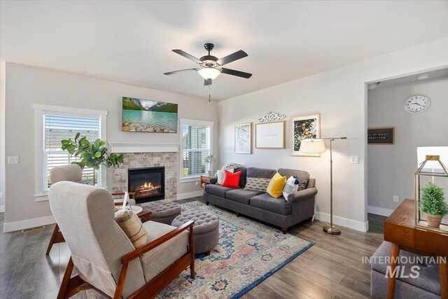 living room featuring wood-type flooring, ceiling fan, and a stone fireplace