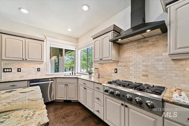 kitchen featuring dark hardwood / wood-style flooring, backsplash, light stone counters, wall chimney exhaust hood, and stainless steel appliances