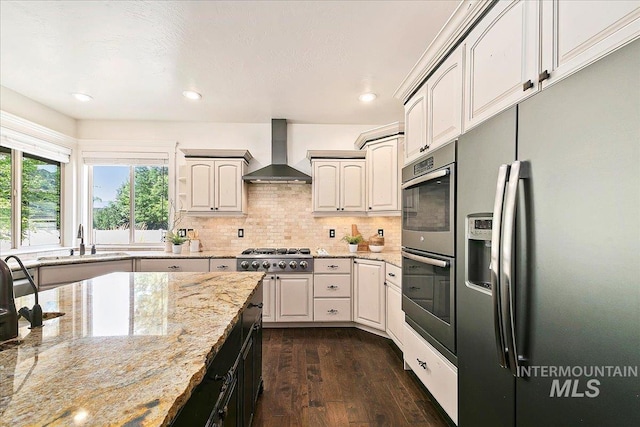 kitchen with wall chimney range hood, sink, light stone countertops, appliances with stainless steel finishes, and dark hardwood / wood-style flooring