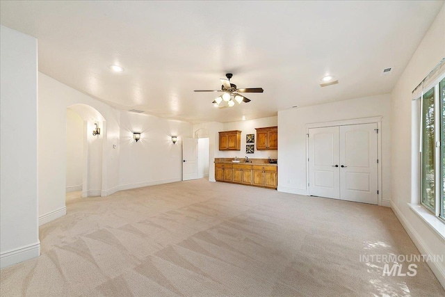 unfurnished living room with light colored carpet, ceiling fan, a healthy amount of sunlight, and sink