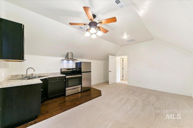 kitchen with wall chimney range hood, sink, vaulted ceiling, appliances with stainless steel finishes, and wood-type flooring