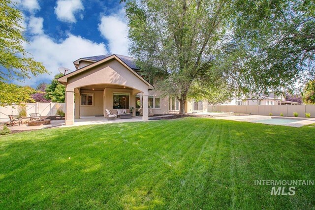 rear view of house with a yard, a fenced in pool, a fire pit, and a patio area