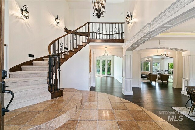 entryway featuring wood-type flooring, ornate columns, ornamental molding, and a high ceiling