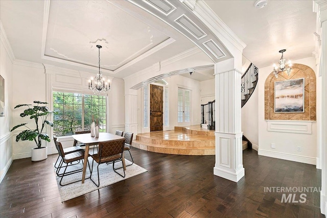 dining room featuring decorative columns, a tray ceiling, crown molding, a notable chandelier, and dark hardwood / wood-style floors