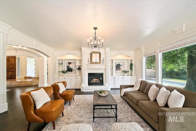 living room featuring built in shelves, hardwood / wood-style floors, ornamental molding, and an inviting chandelier