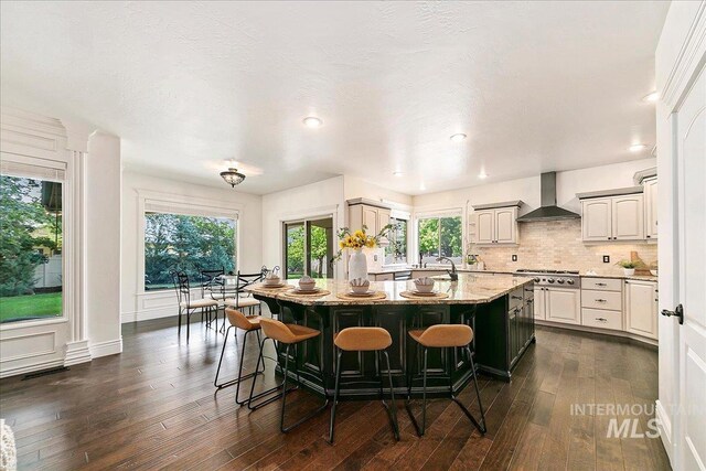 kitchen featuring plenty of natural light, a center island, light stone countertops, and wall chimney range hood