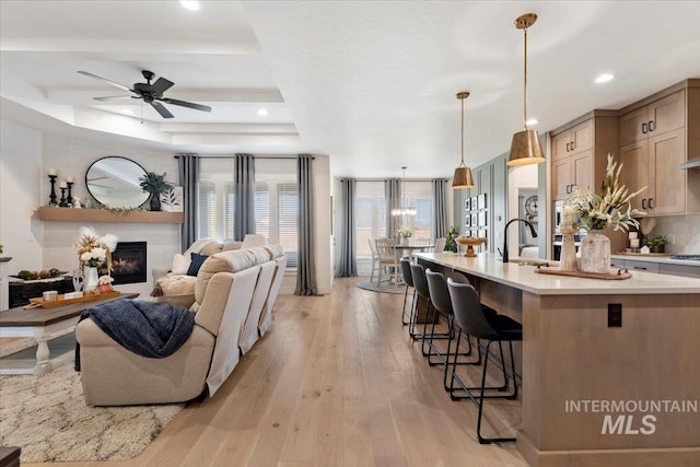 203 S Fusion Ave, Kuna, ID 83634 - living room featuring a glass covered fireplace, light wood finished floors, a ceiling fan, recessed lighting, and a raised ceiling
